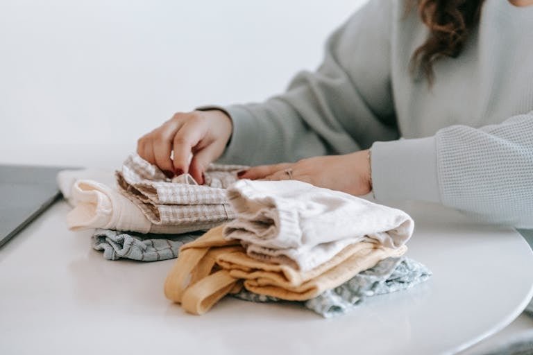 A woman organizing folded clothes on a table at home, emphasizing neatness and lifestyle.